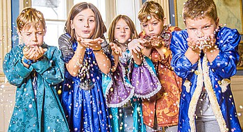 Fünf Kinder in bunten Kostümen pusten Konfetti durch die Luft